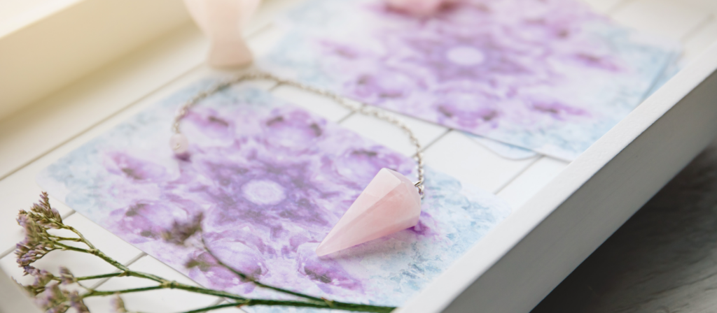Pendule en quartz rose posé sur des cartes oracles violettes
